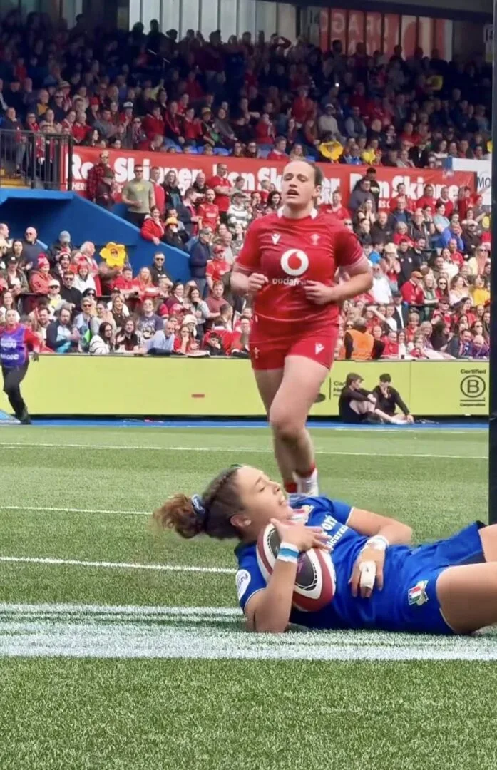 Giocatrice della nazionale italiana femminile di rugby in maglia azzurra sdraiata vicino alla linea di meta con il pallone tra le braccia durante una partita.