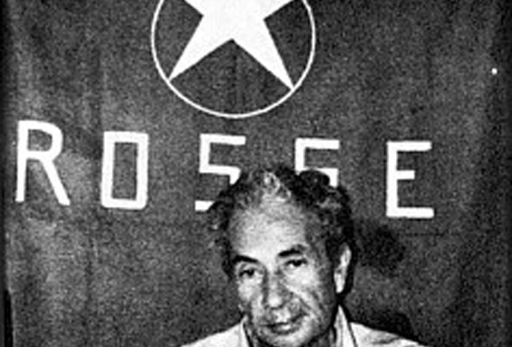 Fotografia storica in bianco e nero di Aldo Moro seduto davanti alla bandiera delle Brigate Rosse durante il sequestro del 1978.