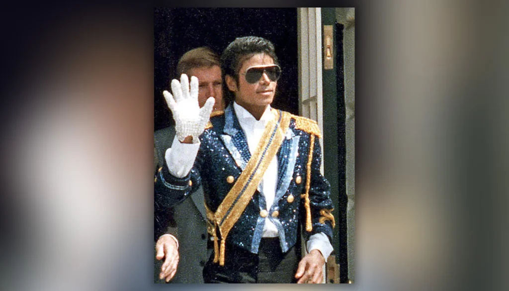 Michael Jackson indossa un abito decorato e saluta con il celebre guanto bianco durante un’apparizione pubblica.