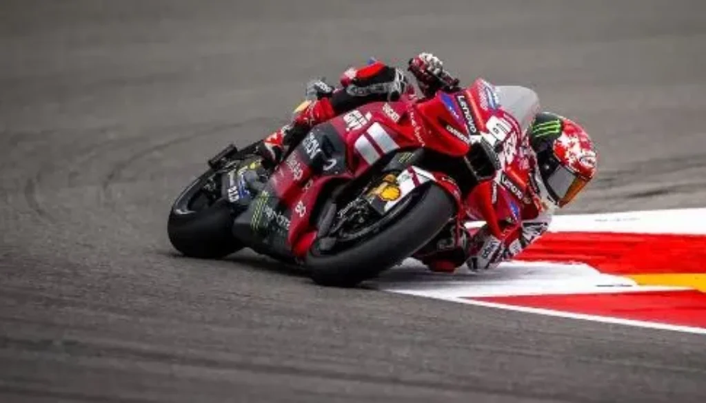 Pilota di MotoGP su una moto Ducati rossa affronta una curva del circuito con una piega molto accentuata vicino al cordolo.