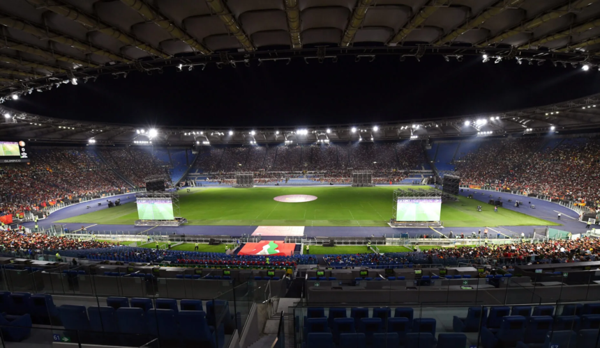 Vista panoramica dello Stadio Olimpico pieno di pubblico durante un evento sportivo serale con il campo illuminato dai riflettori.