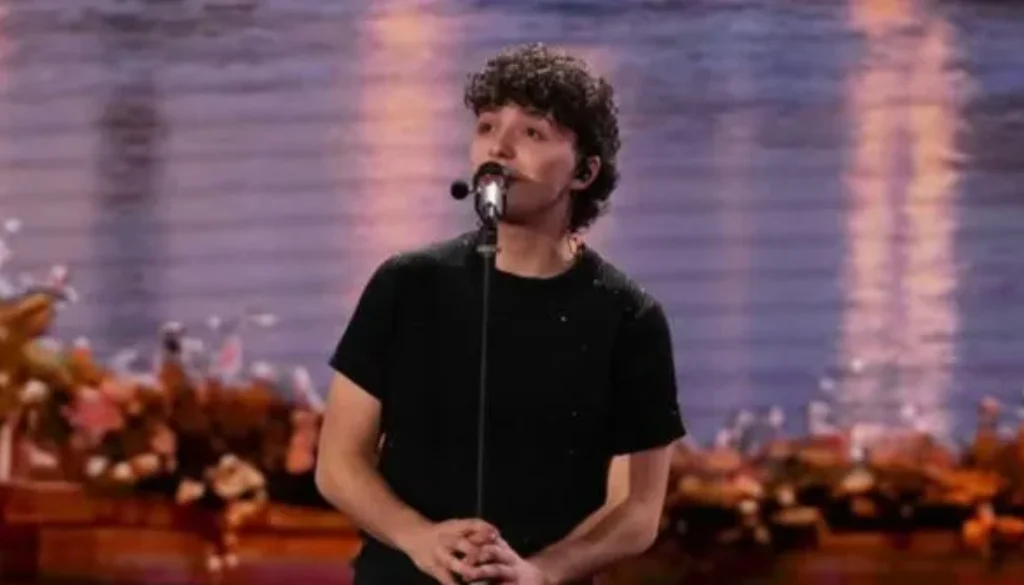 Il cantante Lorenzo Salvetti canta al microfono durante un’esibizione dal vivo su un palco illuminato.