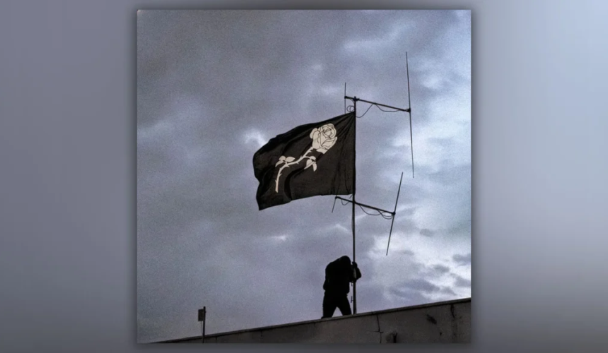 Bandiera nera con una rosa bianca simbolo del progetto musicale Liberato che sventola sotto un cielo nuvoloso.