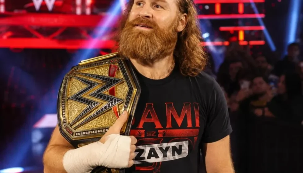 Sami Zayn tiene sulla spalla una cintura di campione WWE durante un evento di wrestling.