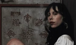 Ritratto artistico di una giovane donna con capelli bicolore seduta davanti a una porta in legno decorata con motivi floreali.