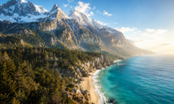 Imponente catena montuosa con cime innevate e boschi rigogliosi affacciata direttamente su una costa rocciosa con spiaggia dorata e mare turchese.