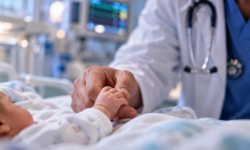 Neonata in ospedale stringe il dito di un medico durante l’assistenza sanitaria.