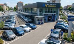 Piazzale esterno di un'agenzia di autonoleggio con diverse automobili parcheggiate sotto tettoie e spazi aperti di fronte a un edificio commerciale moderno