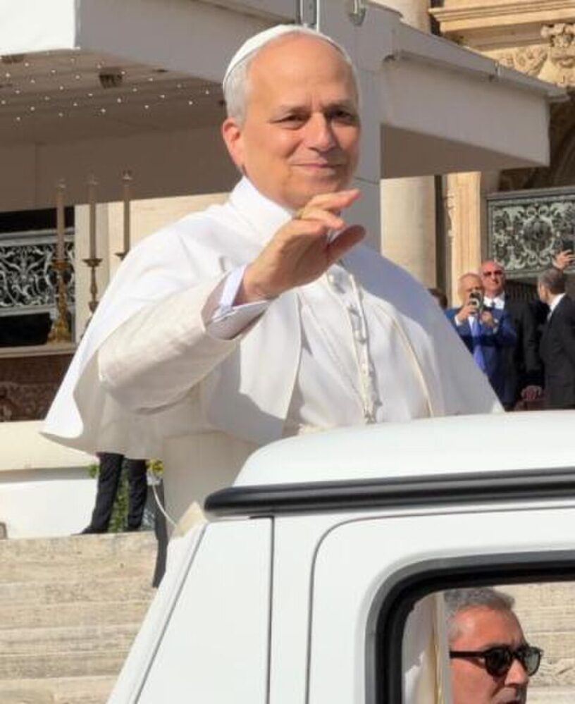 Papa Leone XIV, vestito con l'abito papale bianco, sorride e saluta con la mano i fedeli mentre si trova a bordo della papamobile in Piazza San Pietro, in Vaticano.