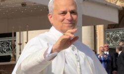 Papa Leone XIV, vestito con l'abito papale bianco, sorride e saluta con la mano i fedeli mentre si trova a bordo della papamobile in Piazza San Pietro, in Vaticano.