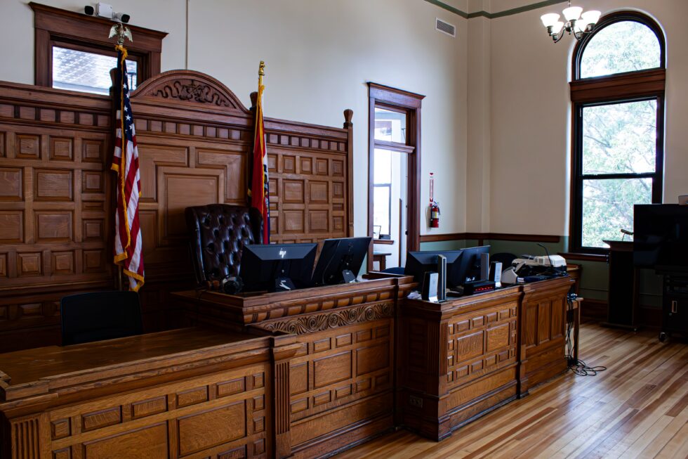 Aula di tribunale americana con banco del giudice in legno, monitor, bandiera degli Stati Uniti e postazioni giudiziarie